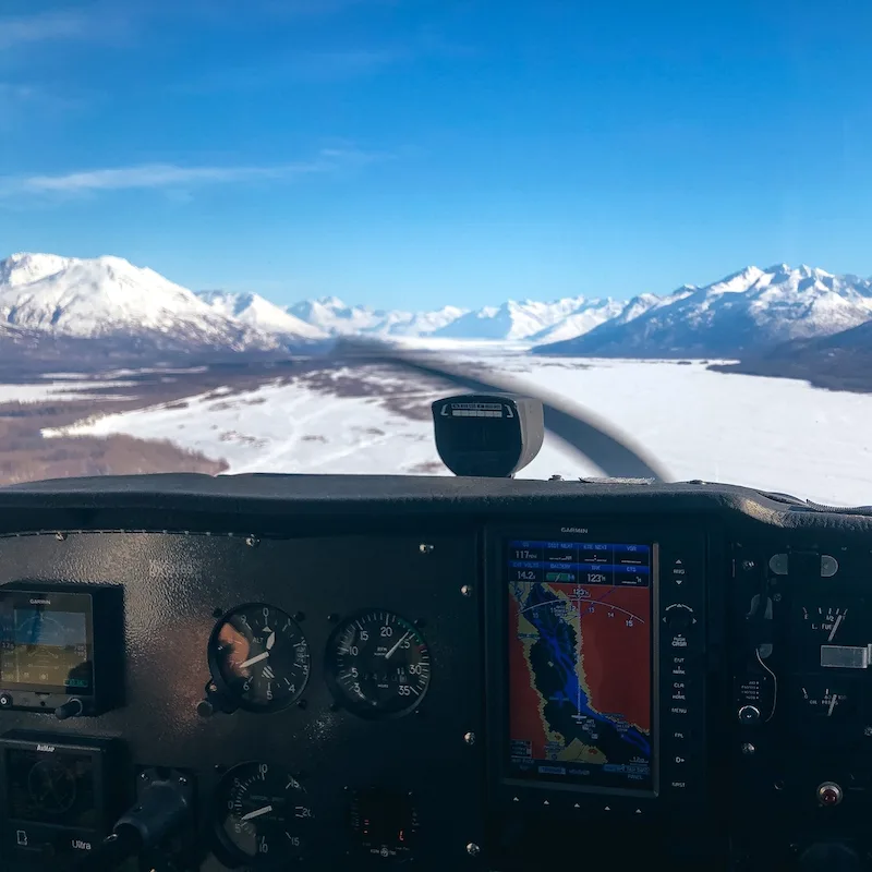 airplane cockpit view flying towards snow capped mountains under blue sky