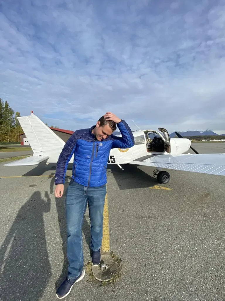aspiring pilot by a plane at alaska flight school, ready for adventure
