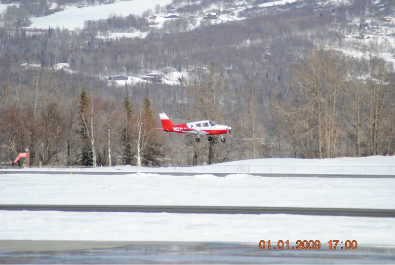 small red white airplane landing on snowy airstrip with trees and houses