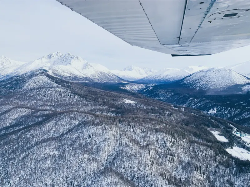 winter flying over snowy mountains and trees from airplane wing view